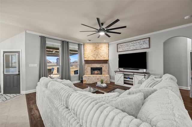 living room featuring dark hardwood / wood-style flooring, crown molding, a stone fireplace, and ceiling fan