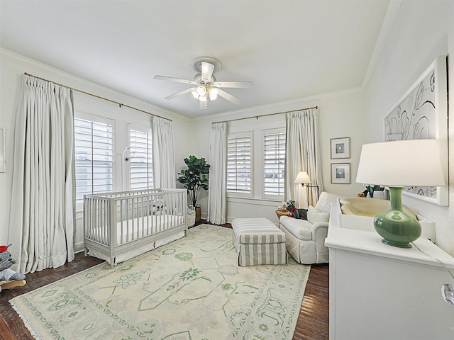 bedroom with a crib, crown molding, dark wood-type flooring, and ceiling fan