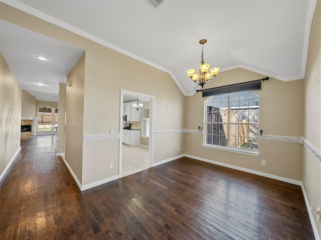 spare room featuring a tiled fireplace, hardwood / wood-style floors, vaulted ceiling, and a chandelier