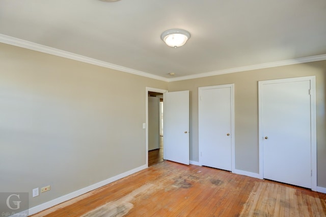 unfurnished bedroom featuring crown molding, light hardwood / wood-style floors, and two closets