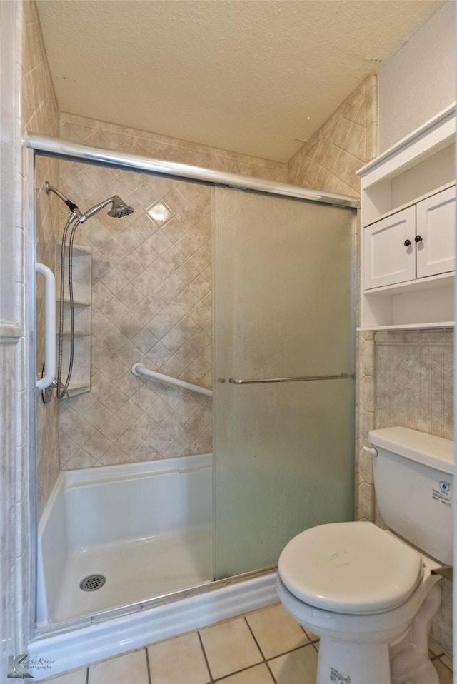 bathroom featuring tile patterned flooring, a shower with door, and toilet