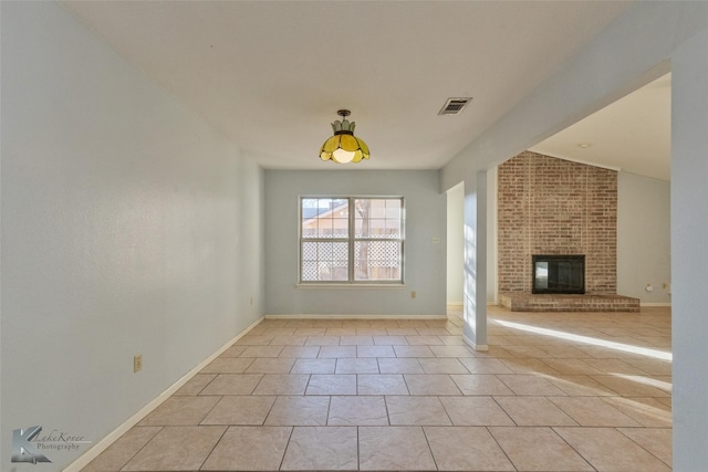 unfurnished living room with vaulted ceiling, a brick fireplace, and light tile patterned floors