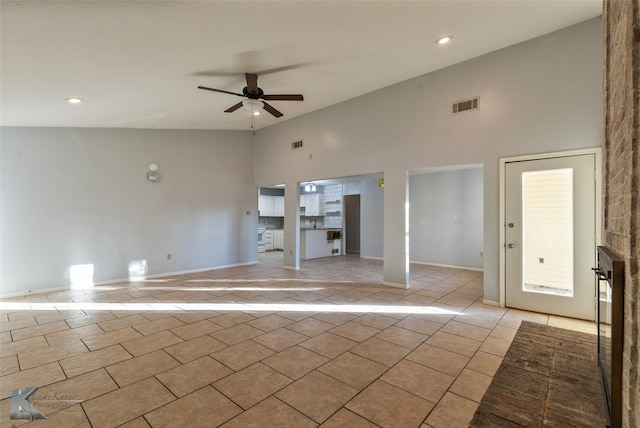 unfurnished living room featuring ceiling fan, a high ceiling, a brick fireplace, and light tile patterned floors