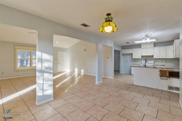 kitchen with light tile patterned floors, backsplash, light stone counters, white cabinets, and kitchen peninsula