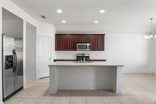 kitchen with a kitchen island with sink, backsplash, stainless steel appliances, light stone counters, and decorative light fixtures