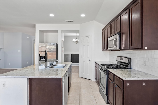 kitchen with sink, appliances with stainless steel finishes, an island with sink, light tile patterned flooring, and decorative backsplash