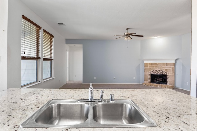 kitchen with ceiling fan, a stone fireplace, sink, and a wealth of natural light