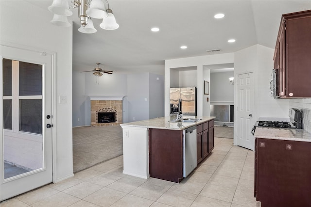 kitchen featuring sink, appliances with stainless steel finishes, an island with sink, pendant lighting, and a fireplace