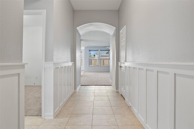 corridor with arched walkways, light colored carpet, light tile patterned flooring, and a textured wall