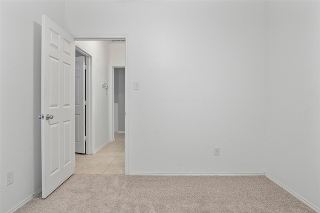 empty room featuring light carpet, light tile patterned floors, and baseboards