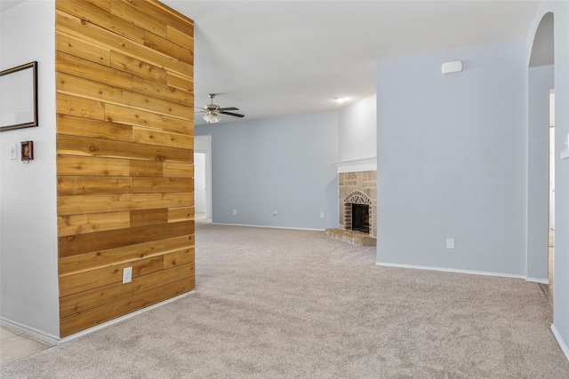 unfurnished living room with ceiling fan, a stone fireplace, light carpet, and wooden walls