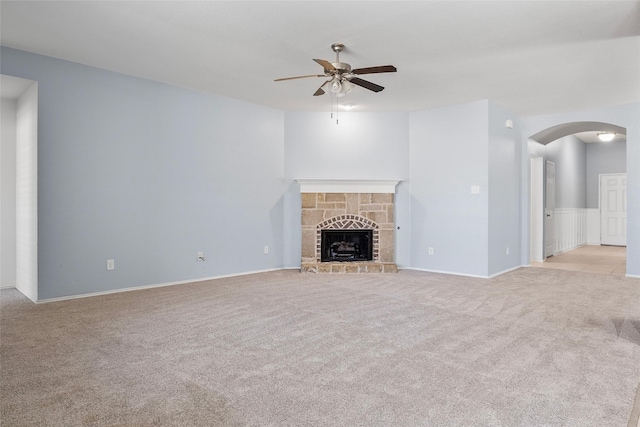 unfurnished living room featuring light carpet, arched walkways, ceiling fan, and a fireplace