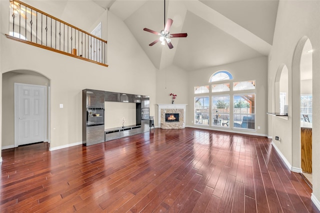 801 Sunrise Dr, Kennedale, TX 76060 - unfurnished living room featuring dark wood-style flooring, baseboards, a ceiling fan, a stone fireplace, and high vaulted ceiling