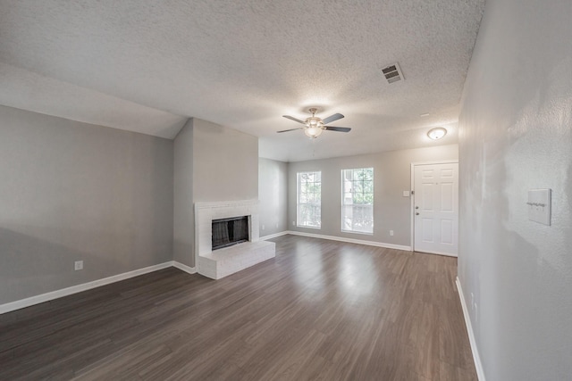 unfurnished living room with a brick fireplace, dark hardwood / wood-style floors, a textured ceiling, and ceiling fan