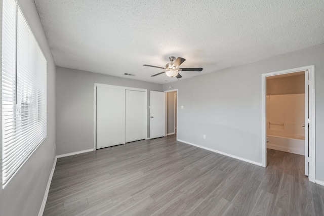 unfurnished bedroom featuring connected bathroom, a textured ceiling, a closet, hardwood / wood-style flooring, and ceiling fan