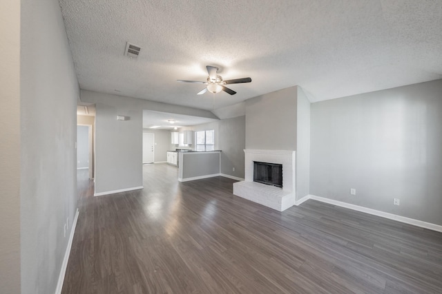 unfurnished living room featuring a brick fireplace, a textured ceiling, dark hardwood / wood-style floors, and ceiling fan