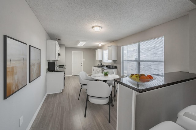 kitchen with a breakfast bar, white cabinets, kitchen peninsula, a textured ceiling, and light hardwood / wood-style flooring