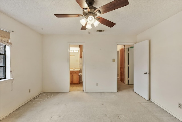 unfurnished bedroom with ensuite bathroom, light colored carpet, a textured ceiling, and ceiling fan