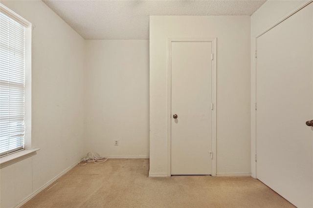 unfurnished bedroom featuring light carpet, multiple windows, and a textured ceiling