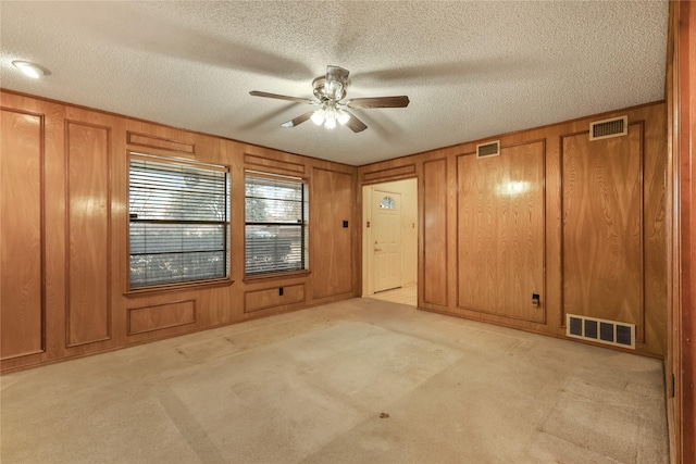 carpeted spare room featuring ceiling fan, a textured ceiling, and wood walls