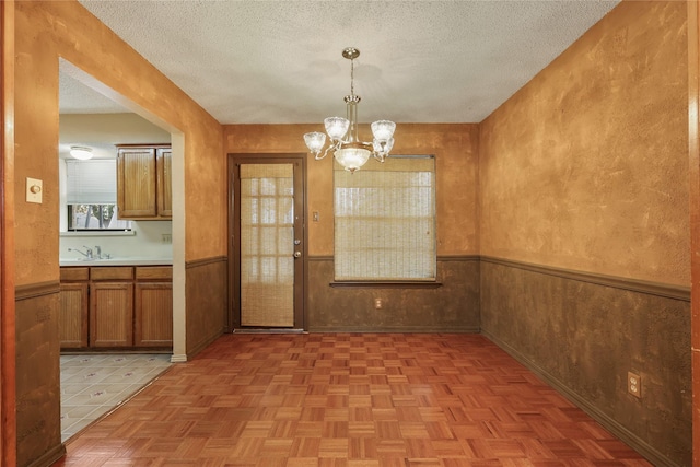 unfurnished dining area with a notable chandelier, a textured ceiling, wooden walls, and light parquet flooring