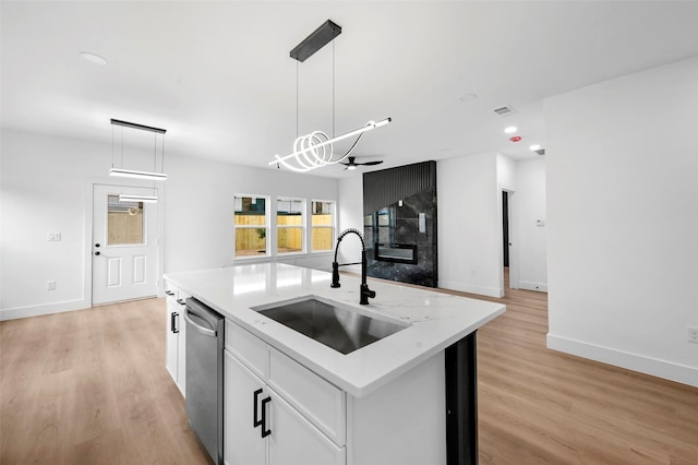 kitchen featuring hanging light fixtures, stainless steel dishwasher, an island with sink, and white cabinets