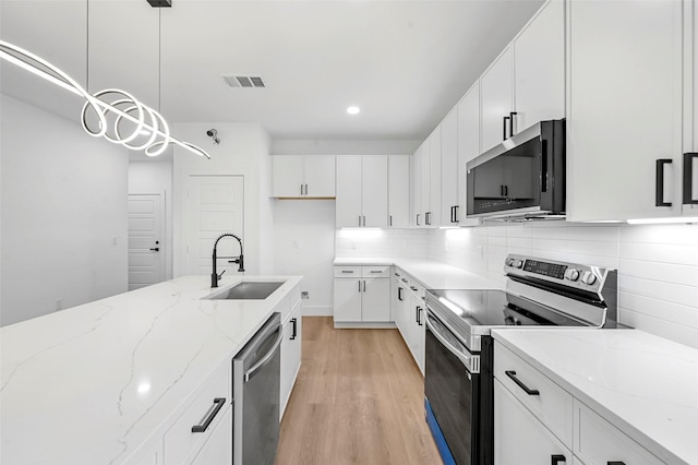 kitchen featuring sink, pendant lighting, stainless steel appliances, light hardwood / wood-style floors, and white cabinets