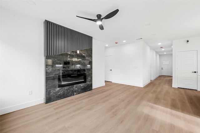 unfurnished living room featuring a tile fireplace, ceiling fan, and light wood-type flooring