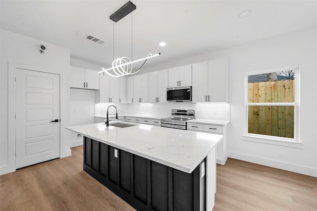 kitchen featuring an island with sink, stainless steel appliances, decorative light fixtures, and sink