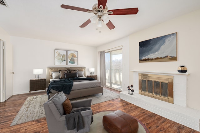 bedroom featuring hardwood / wood-style floors, access to outside, ceiling fan, and a brick fireplace