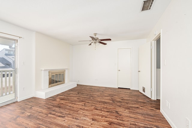 unfurnished living room with a brick fireplace, dark wood-type flooring, and ceiling fan