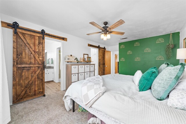 carpeted bedroom with ceiling fan, a barn door, and ensuite bath