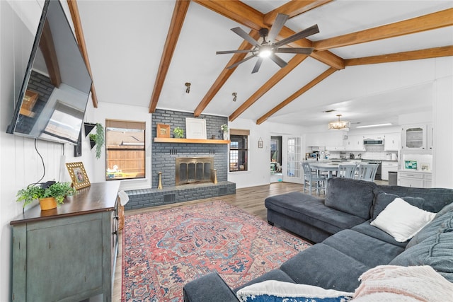 living room featuring ceiling fan with notable chandelier, a fireplace, hardwood / wood-style floors, and vaulted ceiling with beams