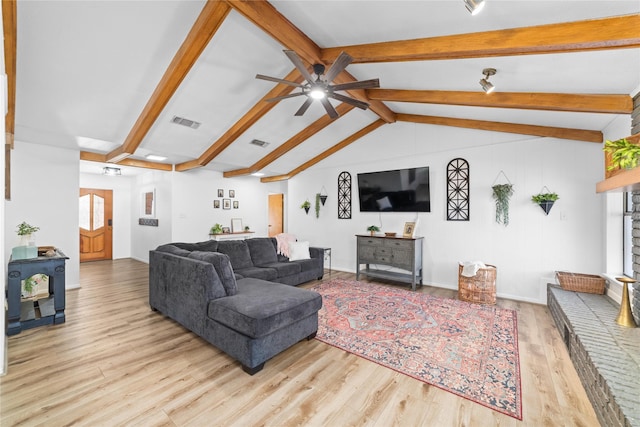 living room with lofted ceiling with beams, ceiling fan, a wood stove, and light wood-type flooring