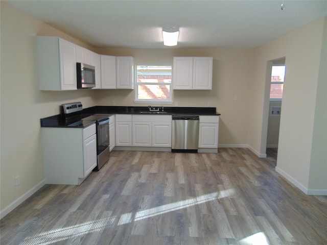 kitchen with stainless steel appliances, sink, white cabinets, and light hardwood / wood-style floors