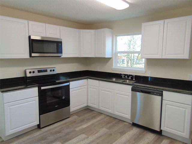 kitchen featuring appliances with stainless steel finishes, white cabinetry, sink, light hardwood / wood-style floors, and a textured ceiling