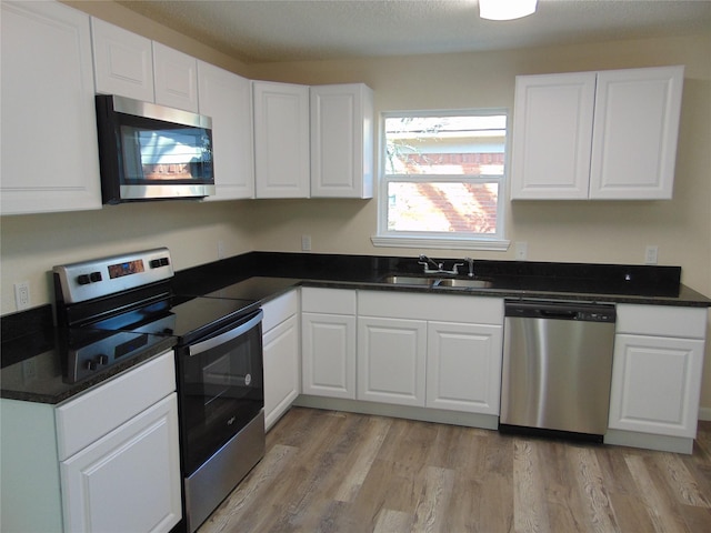 kitchen with stainless steel appliances, sink, white cabinets, and light wood-type flooring