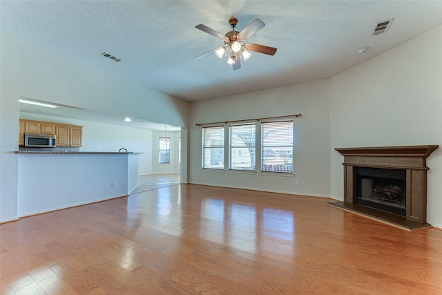 unfurnished living room with ceiling fan, a textured ceiling, and light hardwood / wood-style flooring