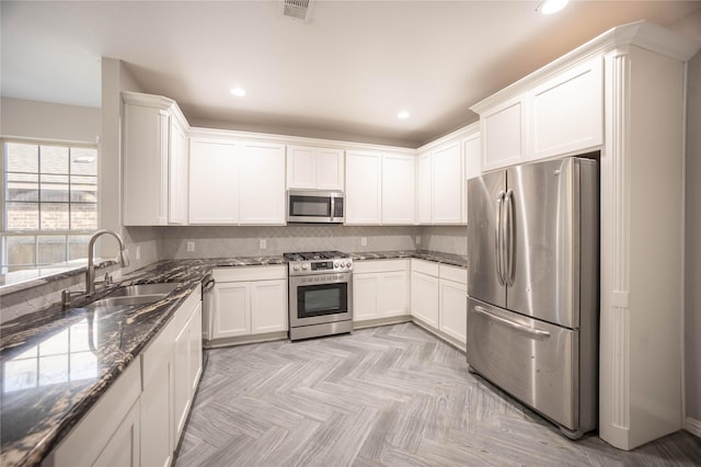 kitchen with appliances with stainless steel finishes, white cabinetry, sink, dark stone countertops, and light parquet flooring