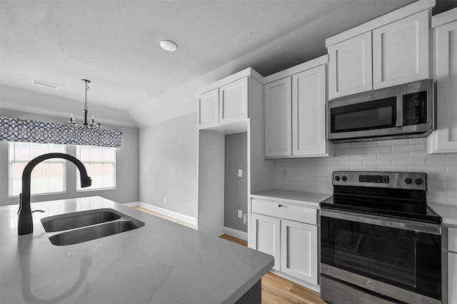 kitchen with visible vents, decorative backsplash, appliances with stainless steel finishes, white cabinetry, and a sink