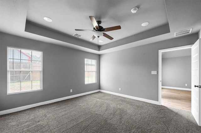 carpeted spare room with a raised ceiling, visible vents, and baseboards