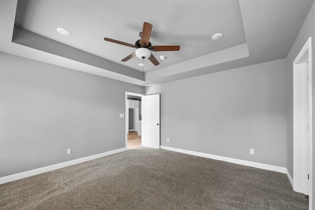 carpeted empty room with a ceiling fan, a tray ceiling, and baseboards