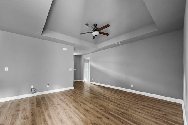 spare room featuring ceiling fan, baseboards, a raised ceiling, and wood finished floors