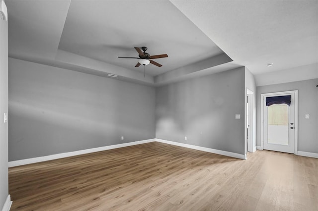 unfurnished room featuring ceiling fan, wood finished floors, visible vents, baseboards, and a tray ceiling