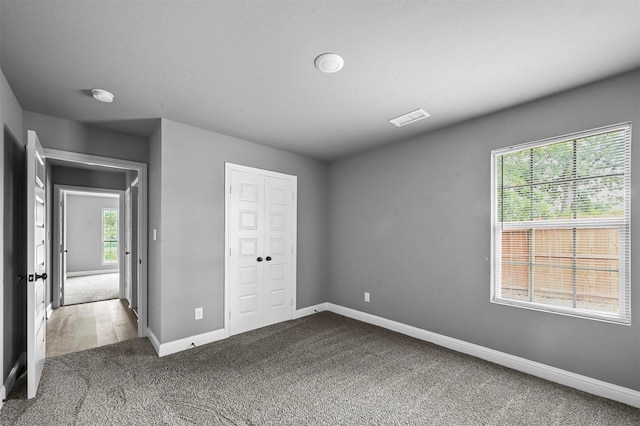 unfurnished bedroom with carpet floors, multiple windows, baseboards, and a closet