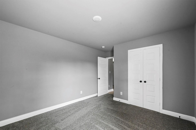 unfurnished bedroom featuring baseboards, dark carpet, and a closet