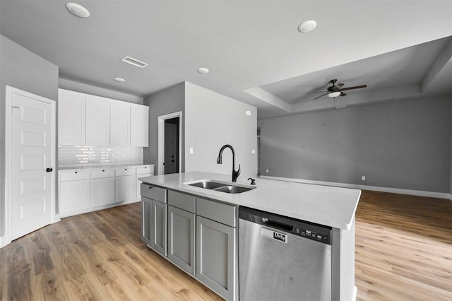 kitchen with a sink, a tray ceiling, white cabinets, and dishwasher