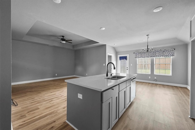 kitchen featuring a sink, baseboards, light wood-style floors, an island with sink, and a raised ceiling