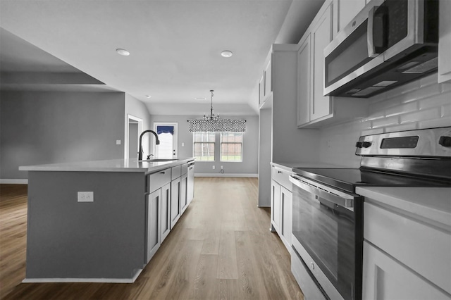 kitchen featuring a center island with sink, light countertops, appliances with stainless steel finishes, a sink, and light wood-type flooring