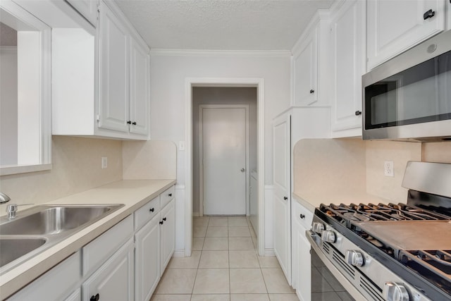 kitchen with sink, light tile patterned floors, ornamental molding, stainless steel appliances, and white cabinets